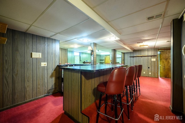 bar with carpet floors, a paneled ceiling, and wood walls