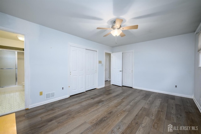 unfurnished bedroom with ceiling fan, dark hardwood / wood-style flooring, and multiple closets