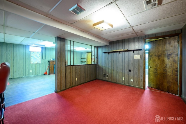 basement with a drop ceiling, carpet flooring, and wooden walls