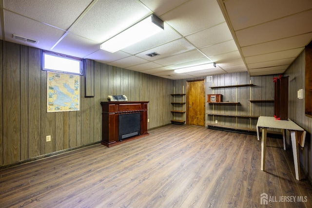 basement with wood walls, hardwood / wood-style floors, and a drop ceiling