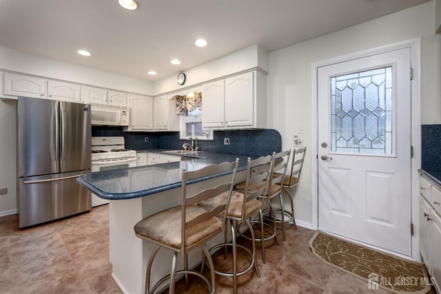 kitchen featuring backsplash, kitchen peninsula, white appliances, a breakfast bar area, and white cabinets