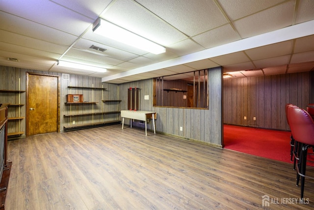 basement featuring wood walls, hardwood / wood-style flooring, and a drop ceiling