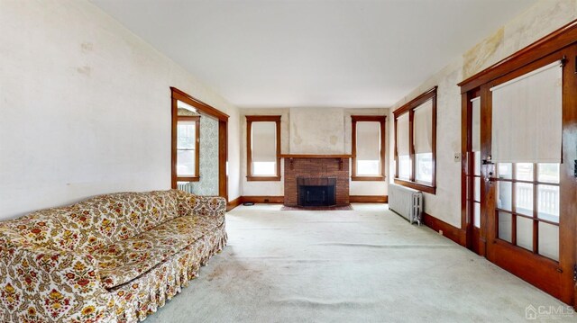 carpeted living room with a fireplace, radiator heating unit, and a wealth of natural light