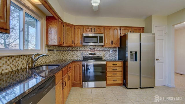 kitchen featuring sink, stainless steel appliances, light tile patterned flooring, decorative backsplash, and dark stone counters