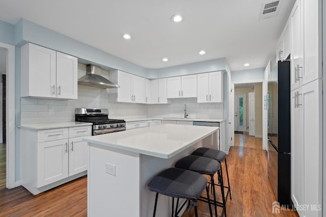 910 Curtis Pl, North Brunswick, NJ 08902 - kitchen with wall chimney exhaust hood, stainless steel appliances, a kitchen breakfast bar, wood finished floors, and white cabinetry
