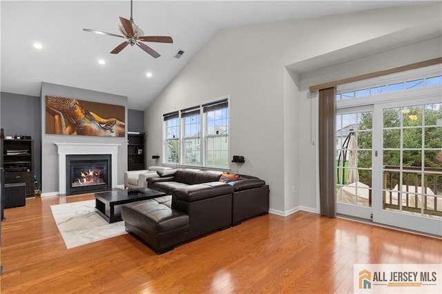 living area with ceiling fan, visible vents, wood finished floors, high vaulted ceiling, and a glass covered fireplace