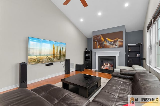 living room featuring ceiling fan, high vaulted ceiling, recessed lighting, a fireplace with flush hearth, and wood finished floors
