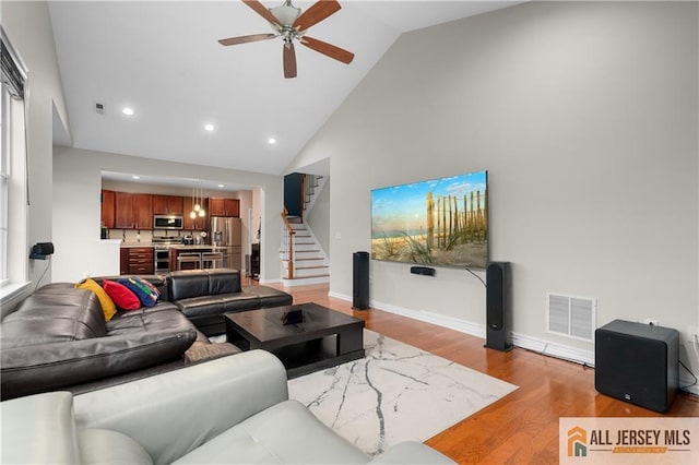 living room with a ceiling fan, visible vents, high vaulted ceiling, stairs, and light wood-style flooring