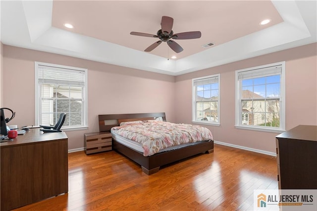 bedroom with light wood-style floors, a raised ceiling, baseboards, and visible vents