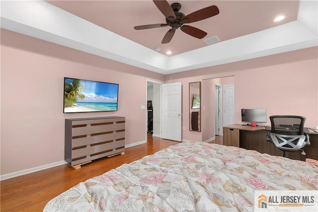 bedroom featuring a raised ceiling, recessed lighting, baseboards, wood finished floors, and visible vents
