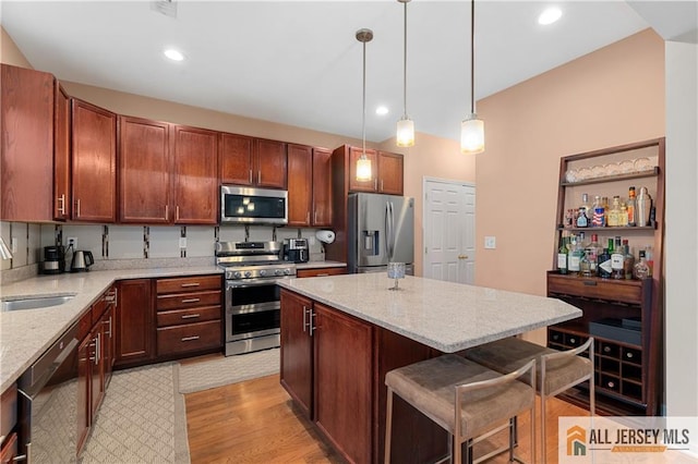 kitchen featuring a kitchen bar, a sink, light wood-style flooring, appliances with stainless steel finishes, and decorative light fixtures