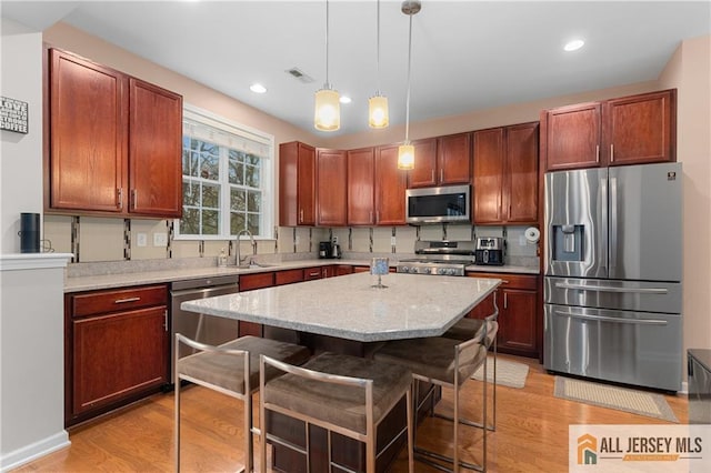 kitchen with a kitchen bar, decorative light fixtures, a center island, light wood-type flooring, and stainless steel appliances