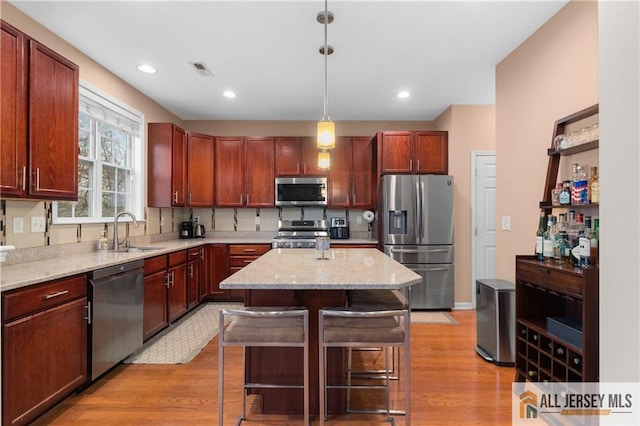 kitchen featuring a kitchen island, a kitchen bar, light wood-type flooring, a sink, and stainless steel appliances