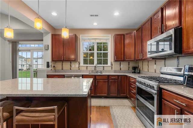 kitchen with a sink, stainless steel appliances, light wood-type flooring, a kitchen bar, and visible vents