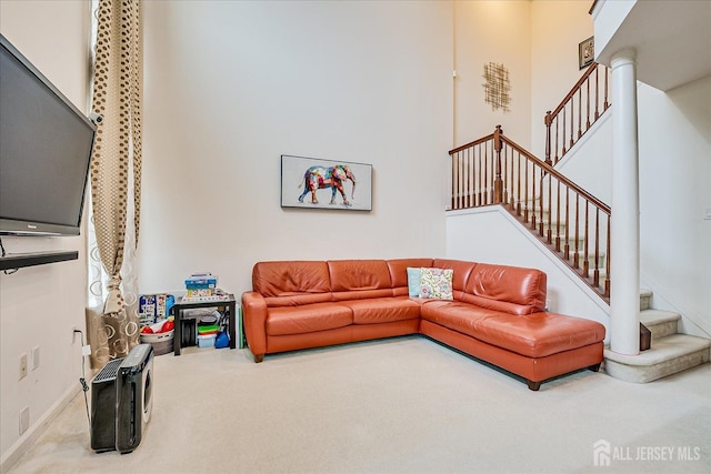 carpeted living area with stairway, a towering ceiling, and baseboards