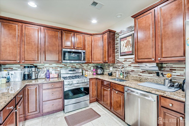 kitchen featuring stainless steel appliances, a sink, tasteful backsplash, light stone countertops, and light tile patterned flooring