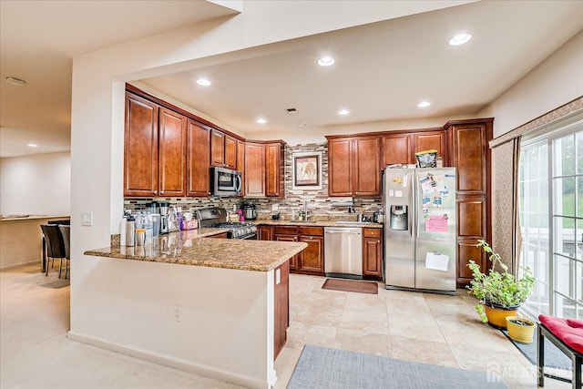 kitchen featuring appliances with stainless steel finishes, a sink, decorative backsplash, brown cabinets, and recessed lighting