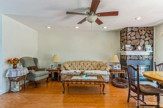 living area with recessed lighting, ceiling fan, wood finished floors, and a stone fireplace