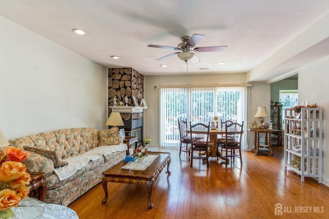 living area with ceiling fan, a stone fireplace, and wood finished floors