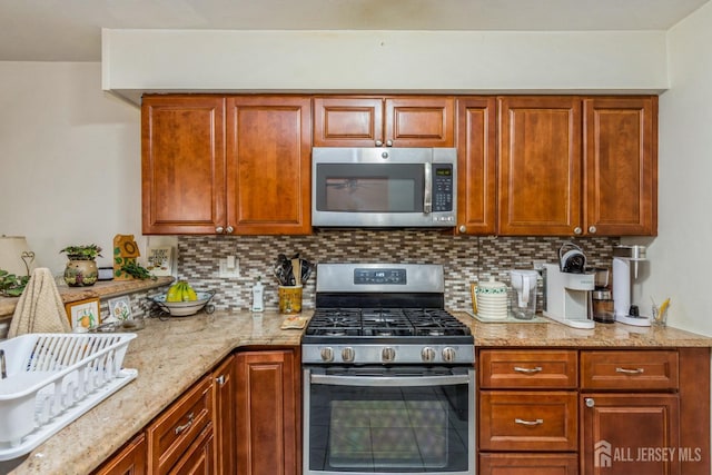 kitchen with appliances with stainless steel finishes, brown cabinets, backsplash, and light stone counters