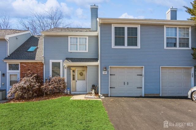 view of front of house featuring driveway, an attached garage, a chimney, and a front lawn