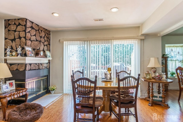 dining space with visible vents, a stone fireplace, baseboards, and wood finished floors