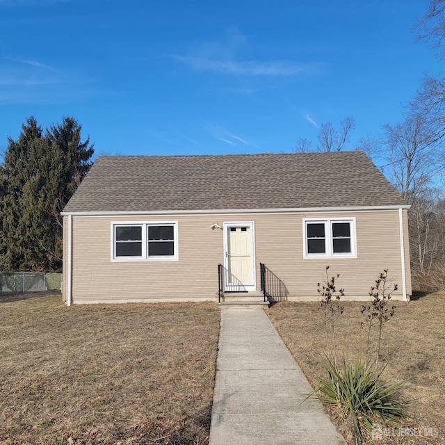 view of front facade with roof with shingles, a front yard, and fence