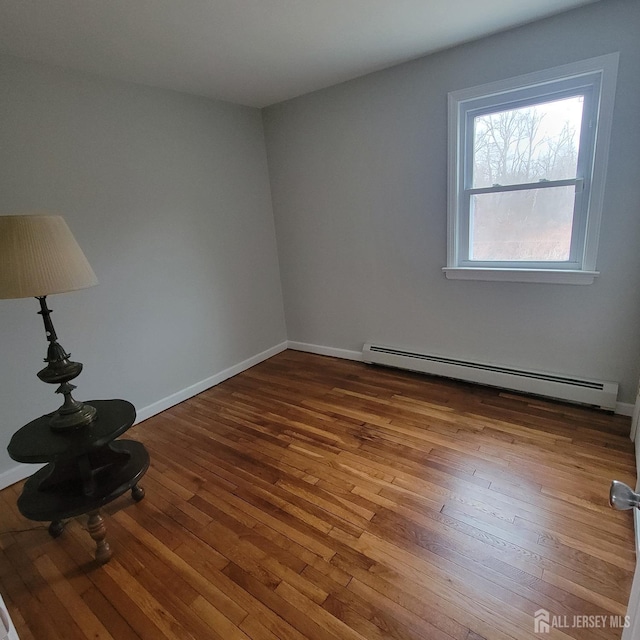 unfurnished room with baseboards, a baseboard radiator, and hardwood / wood-style floors
