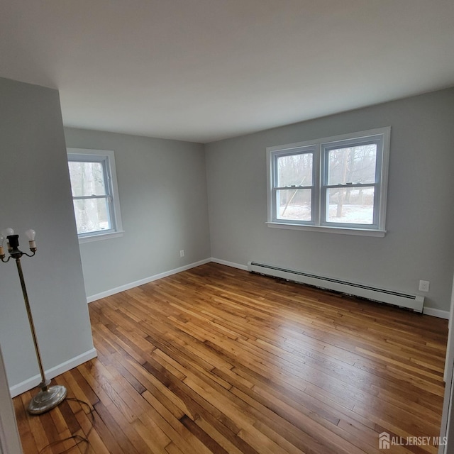 empty room featuring baseboards, a baseboard heating unit, and hardwood / wood-style flooring