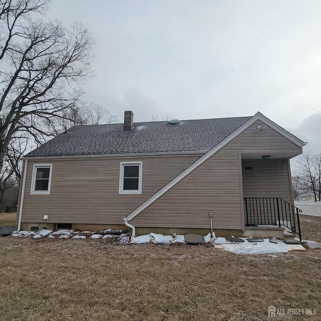 back of house with a yard, a shingled roof, and a chimney