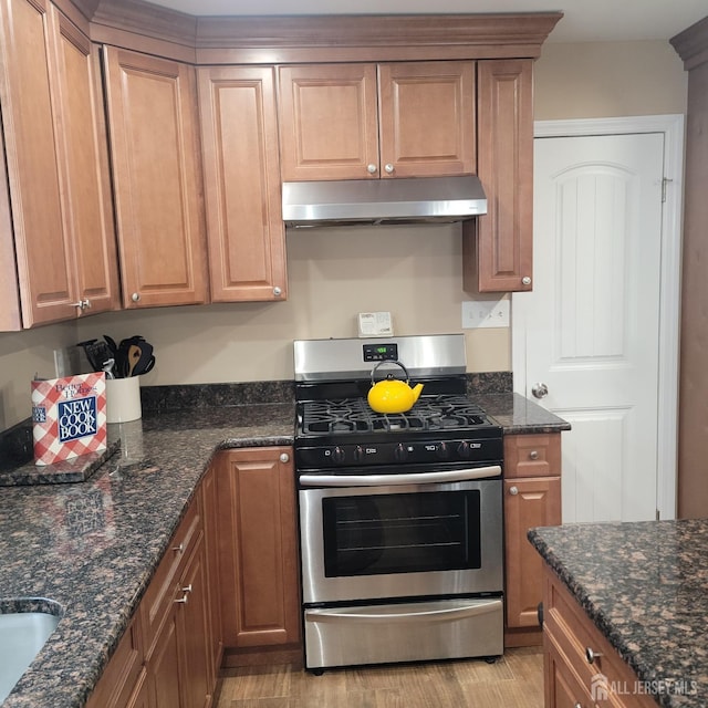 kitchen with dark stone counters, stainless steel gas range oven, under cabinet range hood, and light wood finished floors