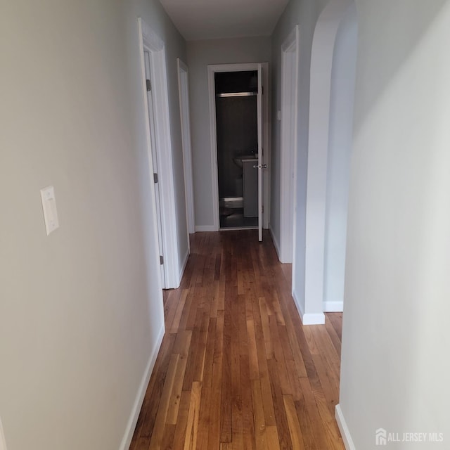 corridor featuring wood-type flooring, arched walkways, and baseboards