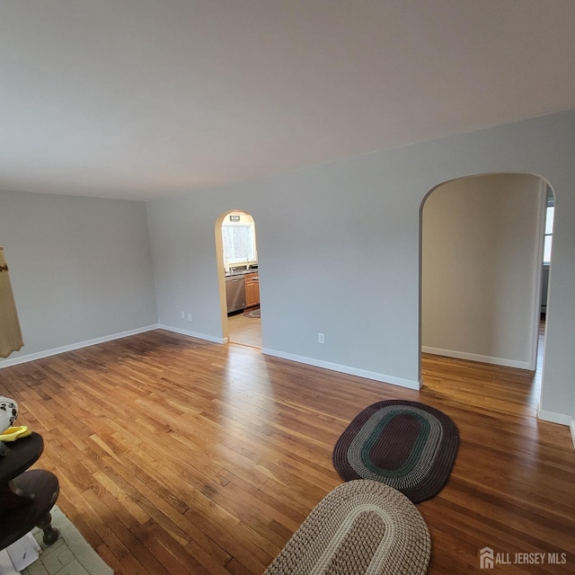unfurnished living room featuring arched walkways, baseboards, and light wood-type flooring