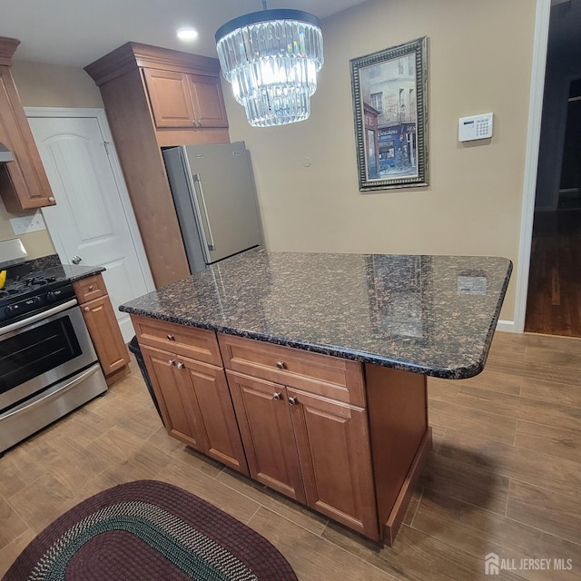 kitchen with dark stone counters, appliances with stainless steel finishes, light wood finished floors, and a notable chandelier