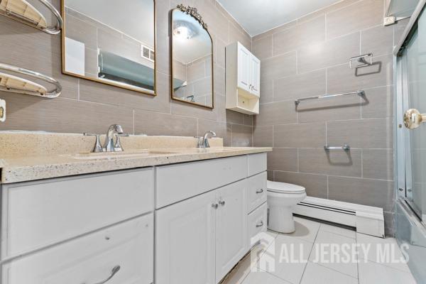 full bathroom with tile patterned floors, vanity, tile walls, and a baseboard heating unit