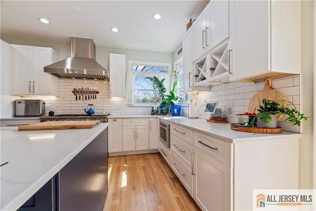 11 Hilltop Blvd N, East Brunswick, NJ 08816 - kitchen with wall chimney range hood, white cabinets, light wood finished floors, recessed lighting, and backsplash