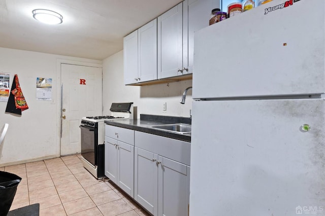 kitchen with gas range oven, sink, light tile patterned floors, white refrigerator, and white cabinets