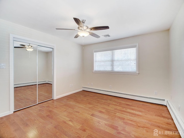 unfurnished bedroom featuring a baseboard heating unit, a closet, a baseboard radiator, and wood finished floors