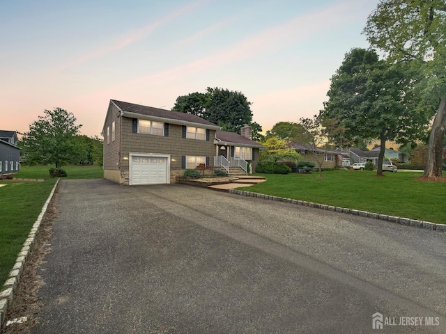 tri-level home with aphalt driveway, an attached garage, and a front lawn