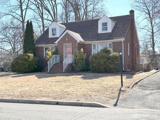 cape cod home featuring a front yard, brick siding, roof with shingles, and a chimney