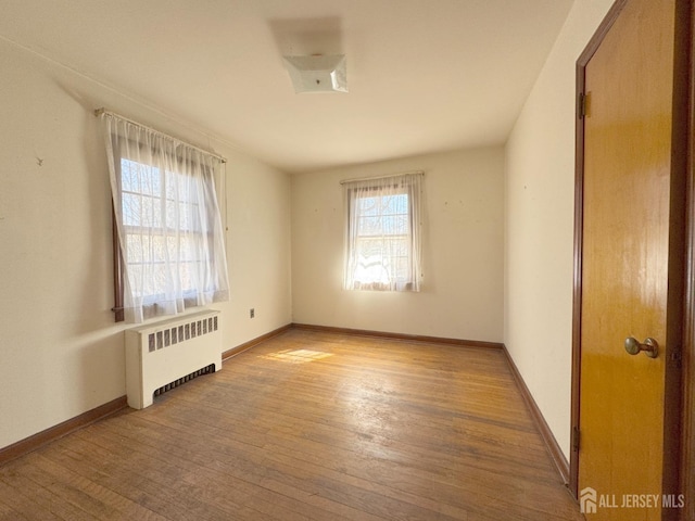 unfurnished room featuring radiator, baseboards, and wood-type flooring