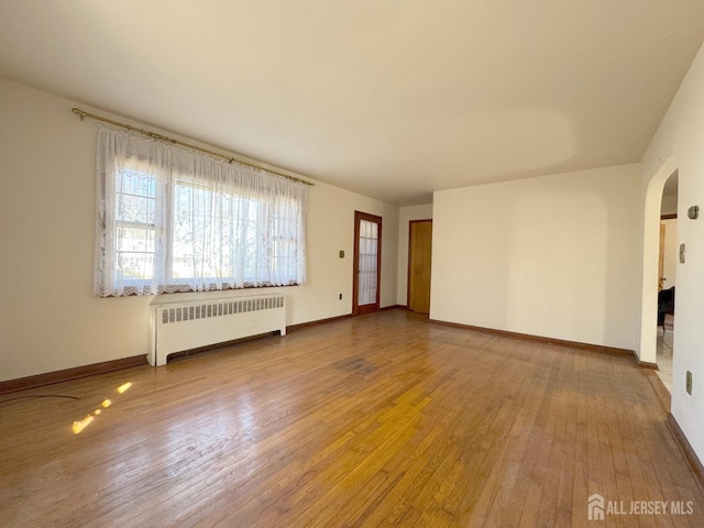 spare room featuring hardwood / wood-style flooring, radiator heating unit, baseboards, and arched walkways