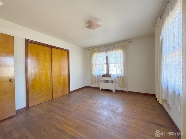 unfurnished bedroom with a closet, radiator, baseboards, and wood finished floors