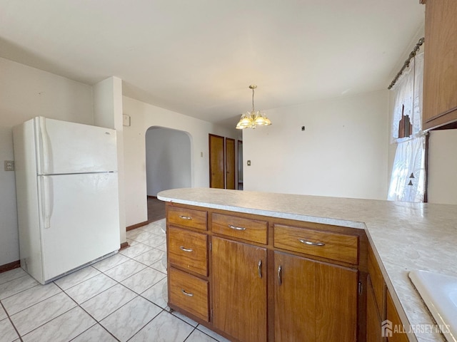 kitchen with arched walkways, brown cabinets, light countertops, and freestanding refrigerator