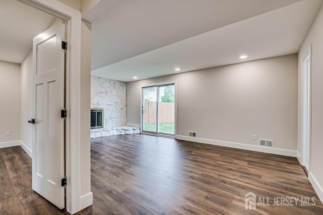 unfurnished living room with dark wood-style flooring, a stone fireplace, baseboards, and recessed lighting