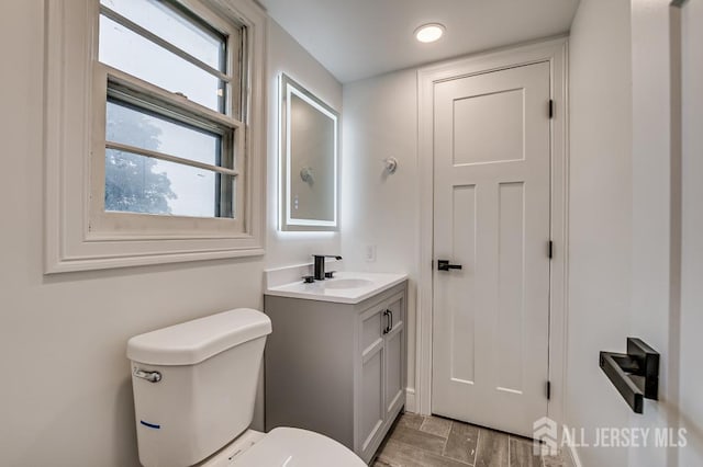 half bath with toilet, vanity, and wood finished floors