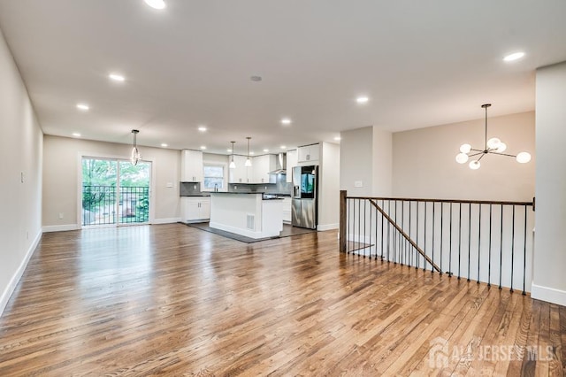 unfurnished living room with a chandelier, wood finished floors, recessed lighting, and baseboards