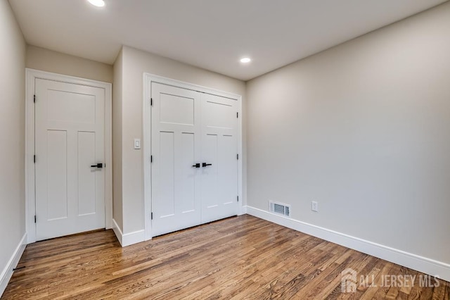 unfurnished bedroom with light wood-type flooring, baseboards, recessed lighting, and a closet