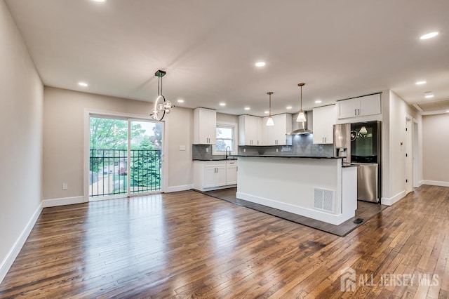 kitchen with wall chimney exhaust hood, stainless steel fridge, dark countertops, dark wood-style flooring, and backsplash