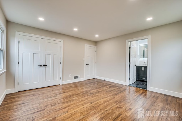 unfurnished bedroom featuring wood finished floors, baseboards, recessed lighting, and connected bathroom